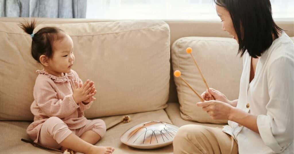 toddler drumming with mom on white sofa