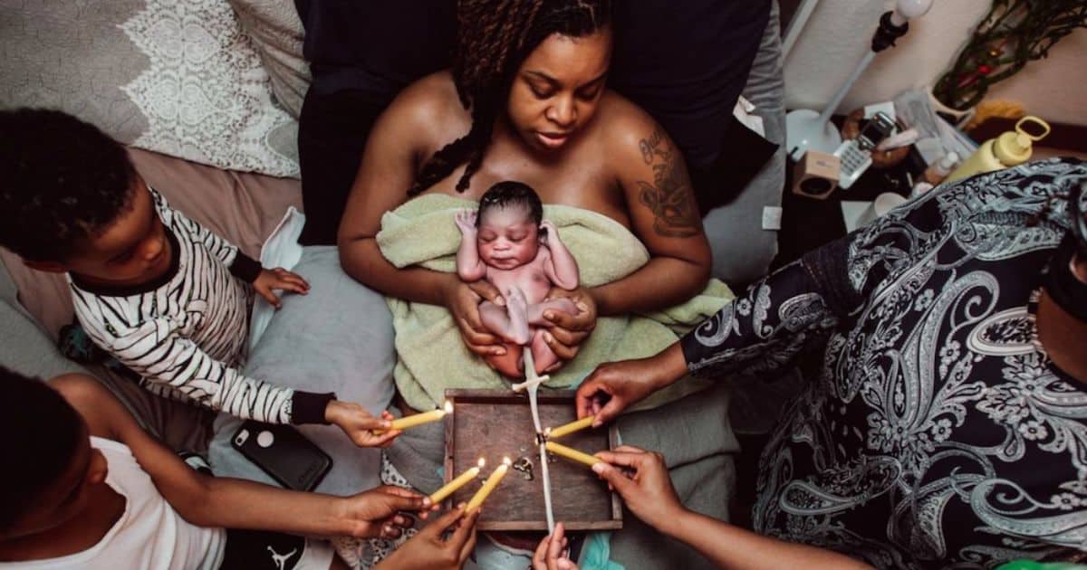 birthing parent with baby on belly and family burning the cord with candles. Nicole Hamic, birth photographer.