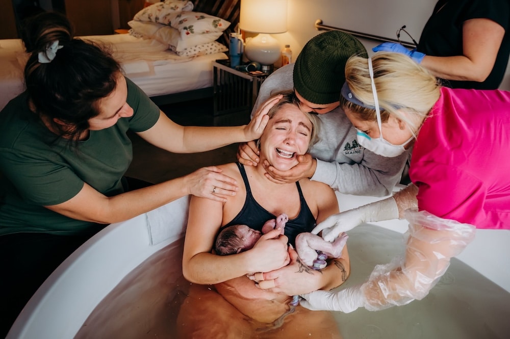home water birth with baby in arms and midwives, doula and partner supporting. 
Nicole Hamic, birth photographer

Birth photography is something that I think a lot of people are unsure about or feel kind of weirded out by. They wonder just how much the photographer will be interrupting the flow of the moment, or if having them there will make the space feel too crowded. Some people are hesitant to spend more on their birth. What I can tell you is that birth photography is NOT someone up in your space with a camera saying “look here!” or stepping in front of your partner to get a shot. And as for cost, I like to think of building your birth support team as one of the single best investments you can make for yourself. As a comparison, if you happen to be married, think about your wedding. What did you spend on your photographer? Your outfit? Cake? Maybe a wedding planner? Odds are you (like most of us) have been culturally conditioned to expect to spend a lot of money on a wedding, and yet our culture doesn’t put the same importance on your birth. 

Birth photographers are incredible at blending into the scenery of a birth space, quietly snapping photos here and there to capture moments that you otherwise wouldn’t remember. They catch the moments of your partner quietly holding your hand, your doula providing counter pressure, and your birth team buzzing around you. They capture the hard work, determination, fatigue, elation, exhaustion, love, and disbelief that you will go through during labor. They capture the first moments with your newborn, as you touch their tiny ears, the fuzz on their shoulders, smell their head, take in their impossibly small fingernails, and catch your partner’s eye with a look of “I can’t believe we did it!” Julie Francom, birth photographer