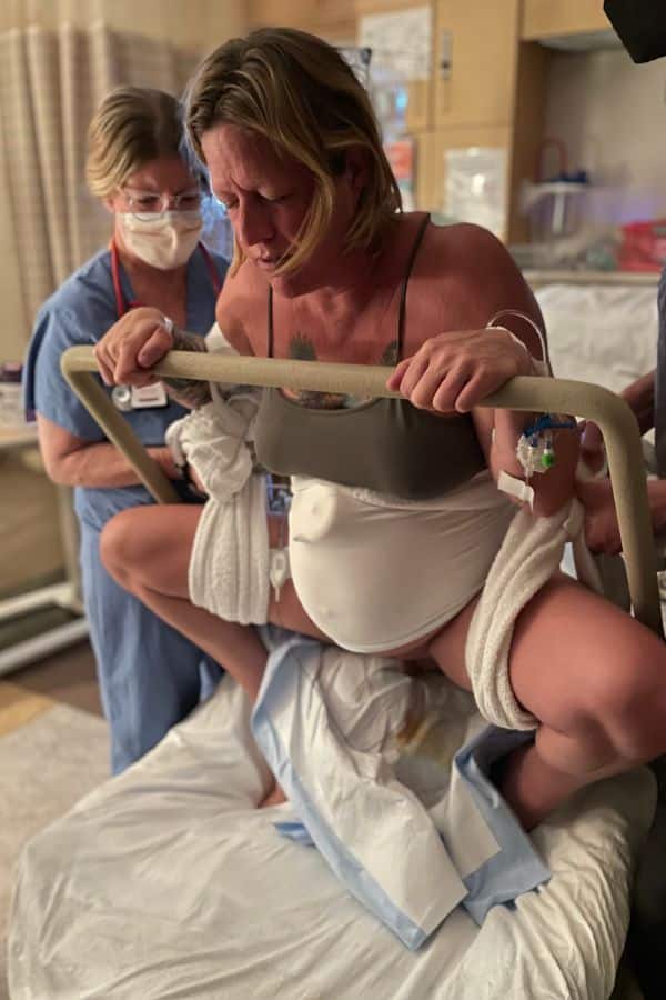Person uses labor squat bar to do an upright squat in her hospital bed