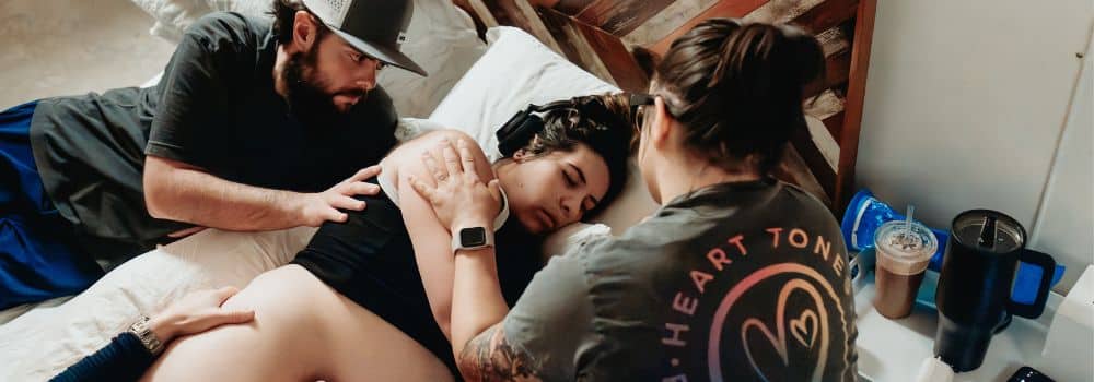 Birthing person in side laying position in labor with doula and partner supporting
