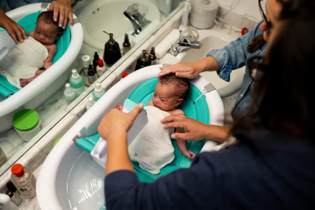 postpartum doula and new mom giving newborn baby a bath