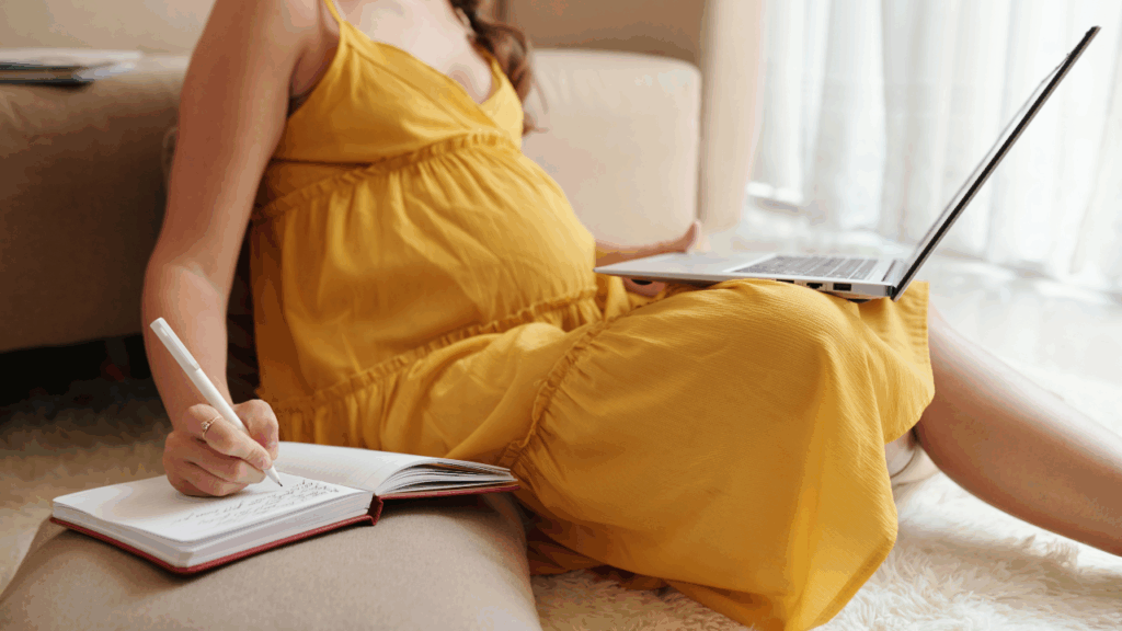 pregnant person on a laptop with a journal